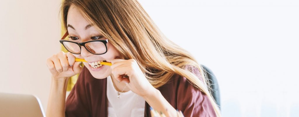 Female with frustrated expression biting pencil looking at laptop