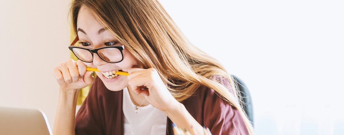 Female with frustrated expression biting pencil looking at laptop