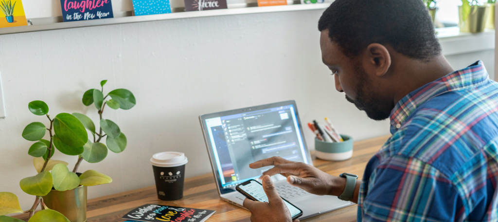 Male sitting at desk with laptop open checking his phone