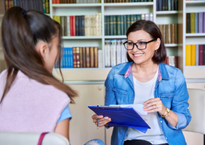 Two women chatting in an office and smiling, backdrop of books on a shelf
