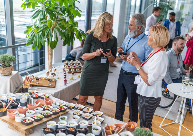 A group of smiling people networking with a buffet and drinks in an events/office space
